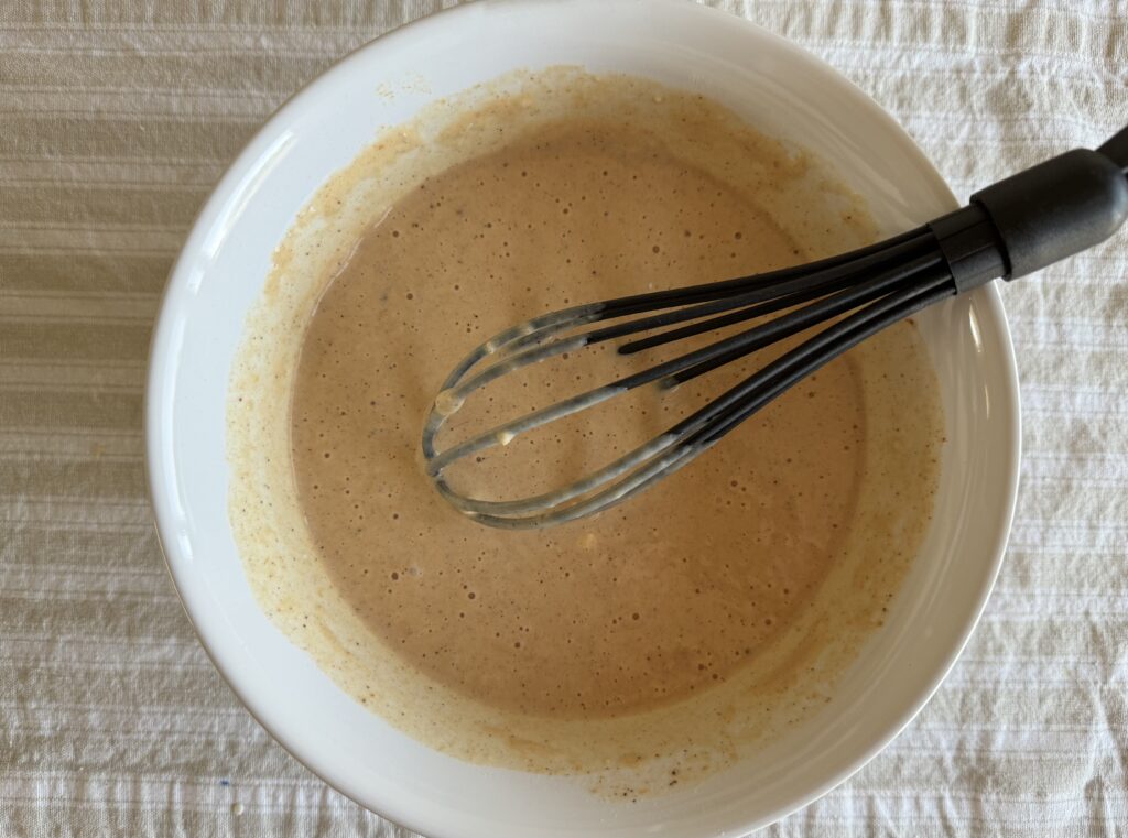 pumpkin spice waffle batter mixed in a ceramic bowl with a black whisk sitting on a table cloth