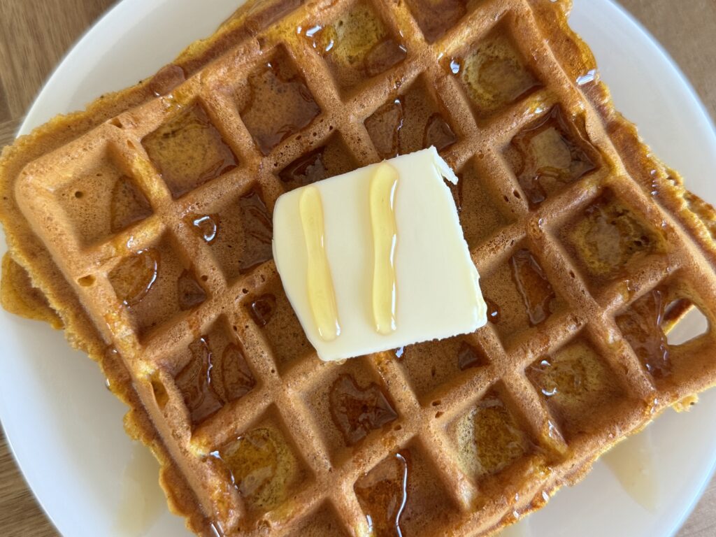pumpkin spice sourdough discard waffle on a plate with a square of butter and a drizzle of honey