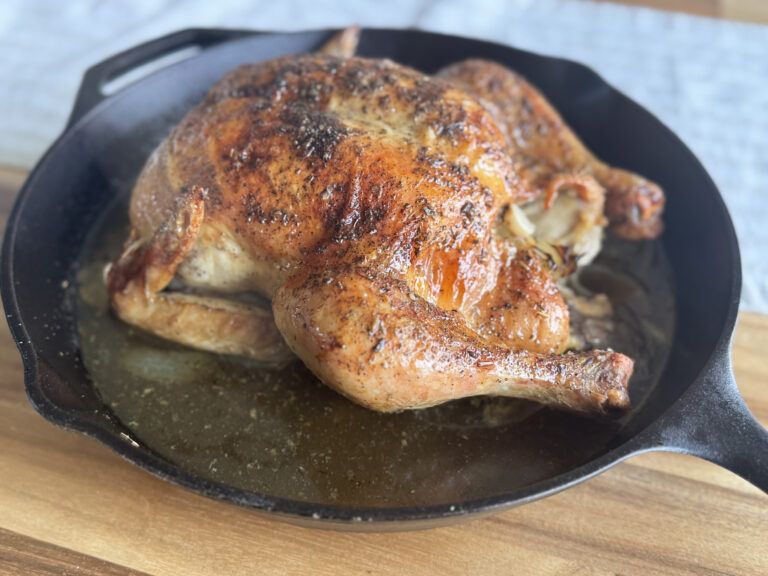 a whole chicken, roasted in a cast iron skillet on a wooden tabletop