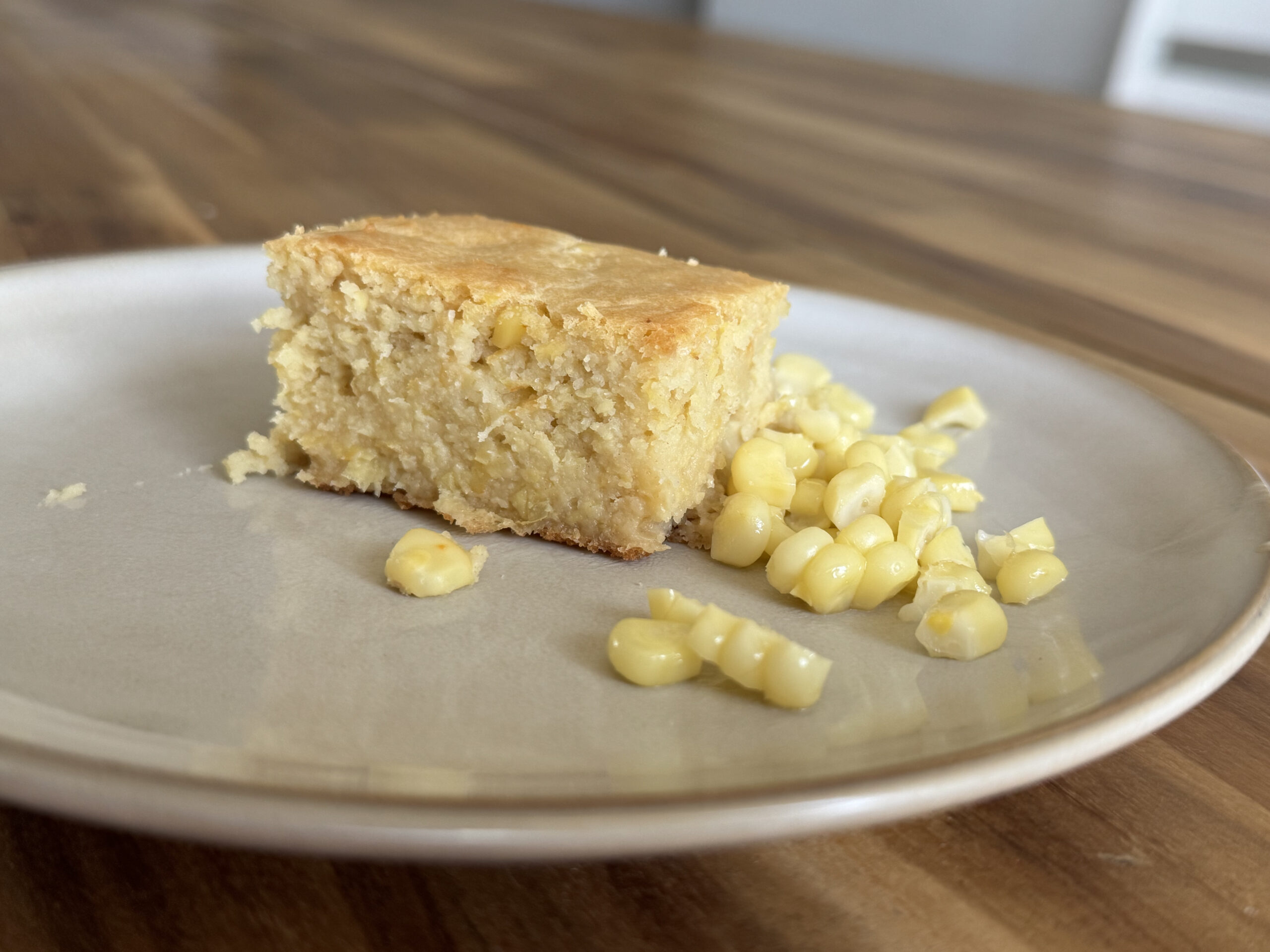 fresh baked cornbread on a plate on a wooden table top with corn next to the cornbread