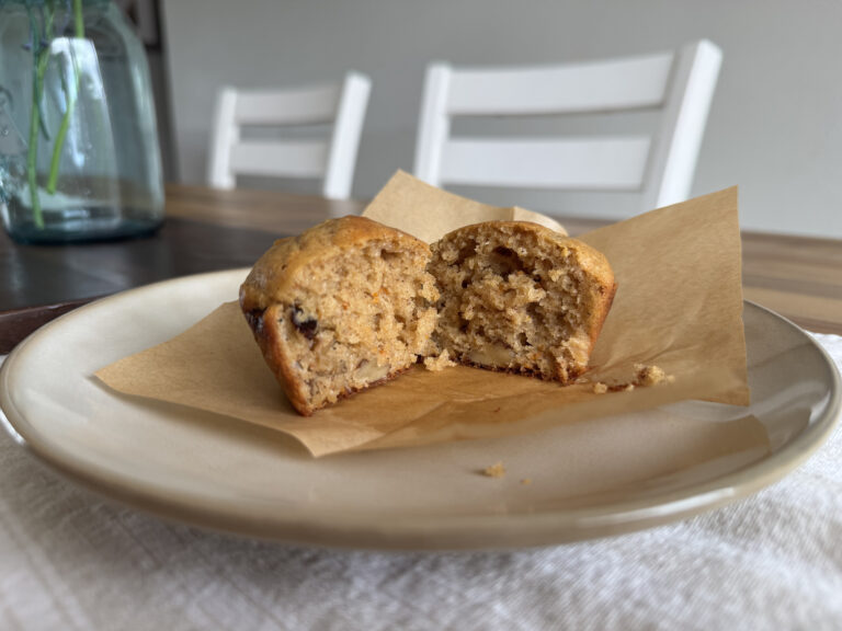 a muffin cut in half on a plate on a wooden table with a flower mason jar in the background.