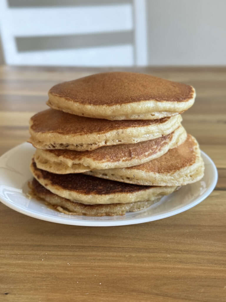 a stack of pancakes on a white plate on a wooden table