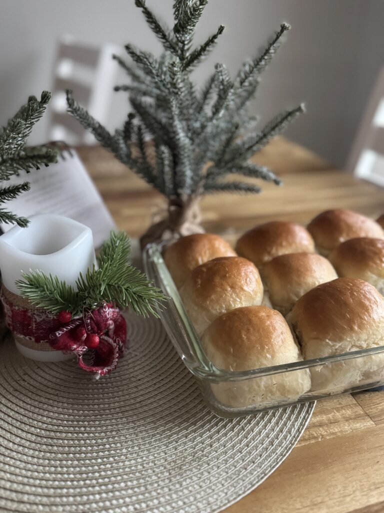 a glass pan of fresh sourdough discard rolls on a wooden table top, with a green tree and a candle.