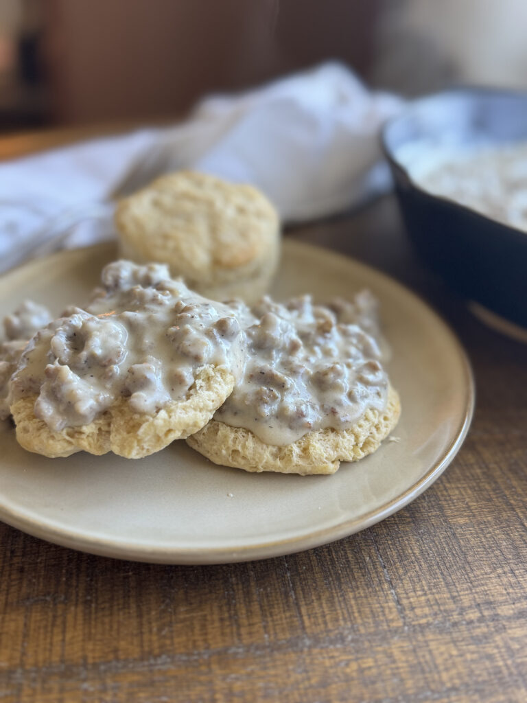 a wooden table with homemade biscuits on a plate with sausage gravy on top.