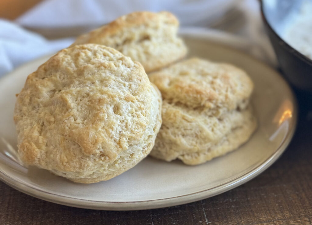 a plate of sourdough discard biscuits on a table with a cast iron pan and a white towel part in the photo.