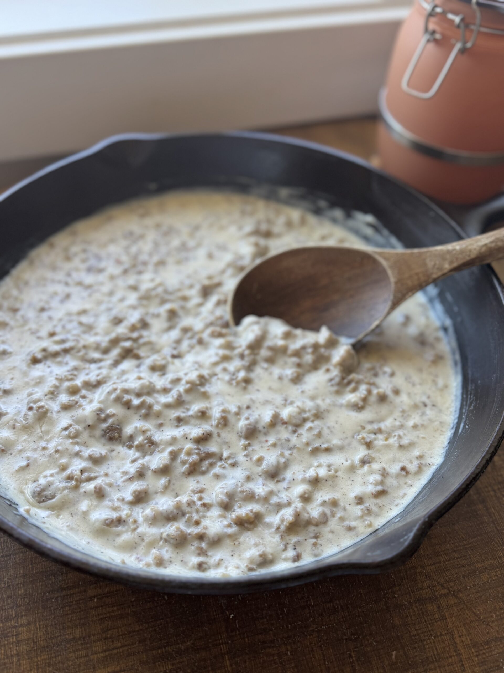 a Cast iron pan full of sausage gravy and a wooden spoon on a wooden table