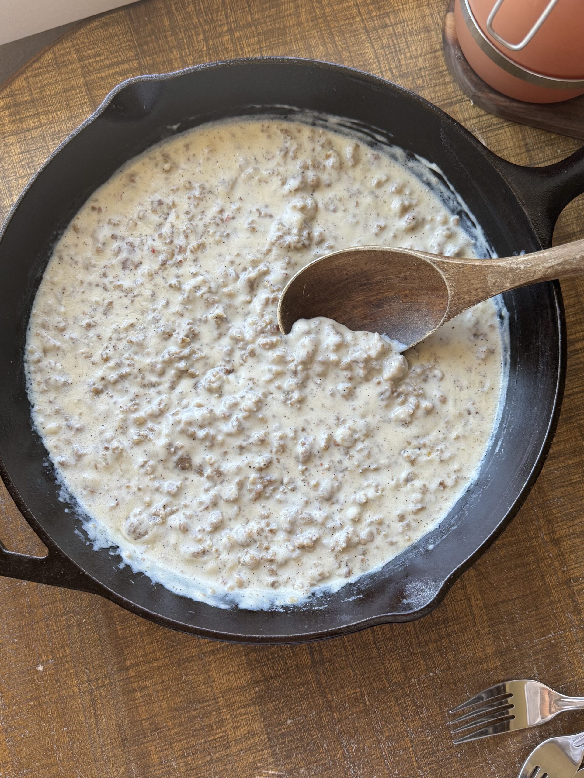 A cast iron pan of country sausage gravy on a wooden table with a wooden spoon