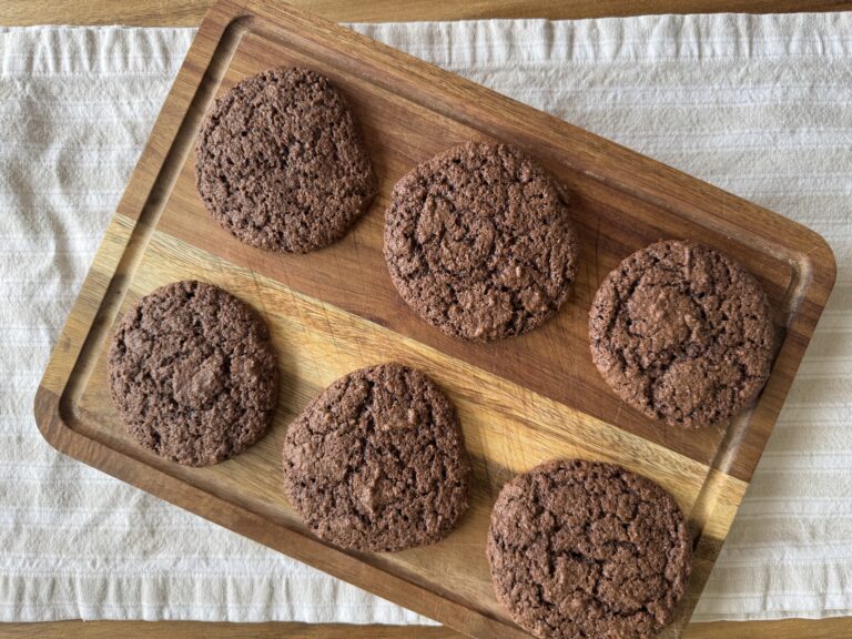 fresh milled sourdough chocolate cookies on a cutting board, fresh out of the oven. Placed on a table with a tan striped table cloth underneath