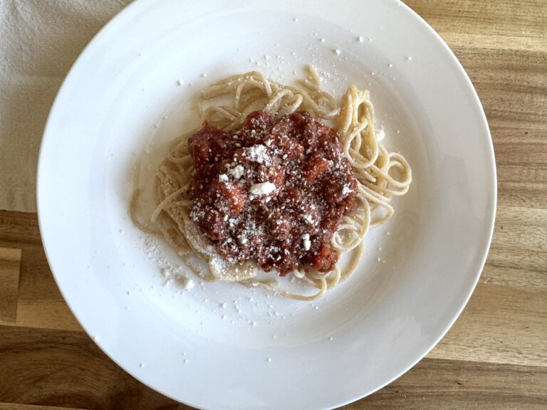 white plate with spaghetti sauce on noodles with parmesan cheese on top on a wooden table