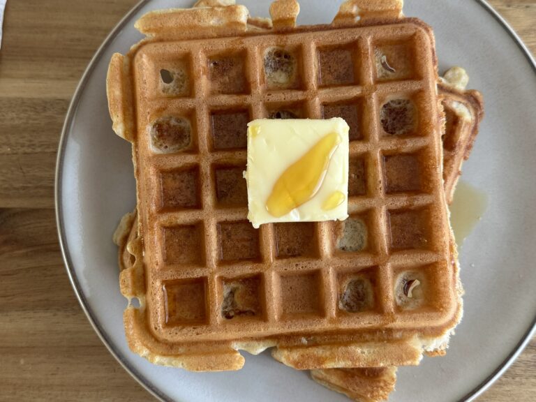 stacked sourdough discard waffles on a plate with a square of butter in the middle with maple syrup