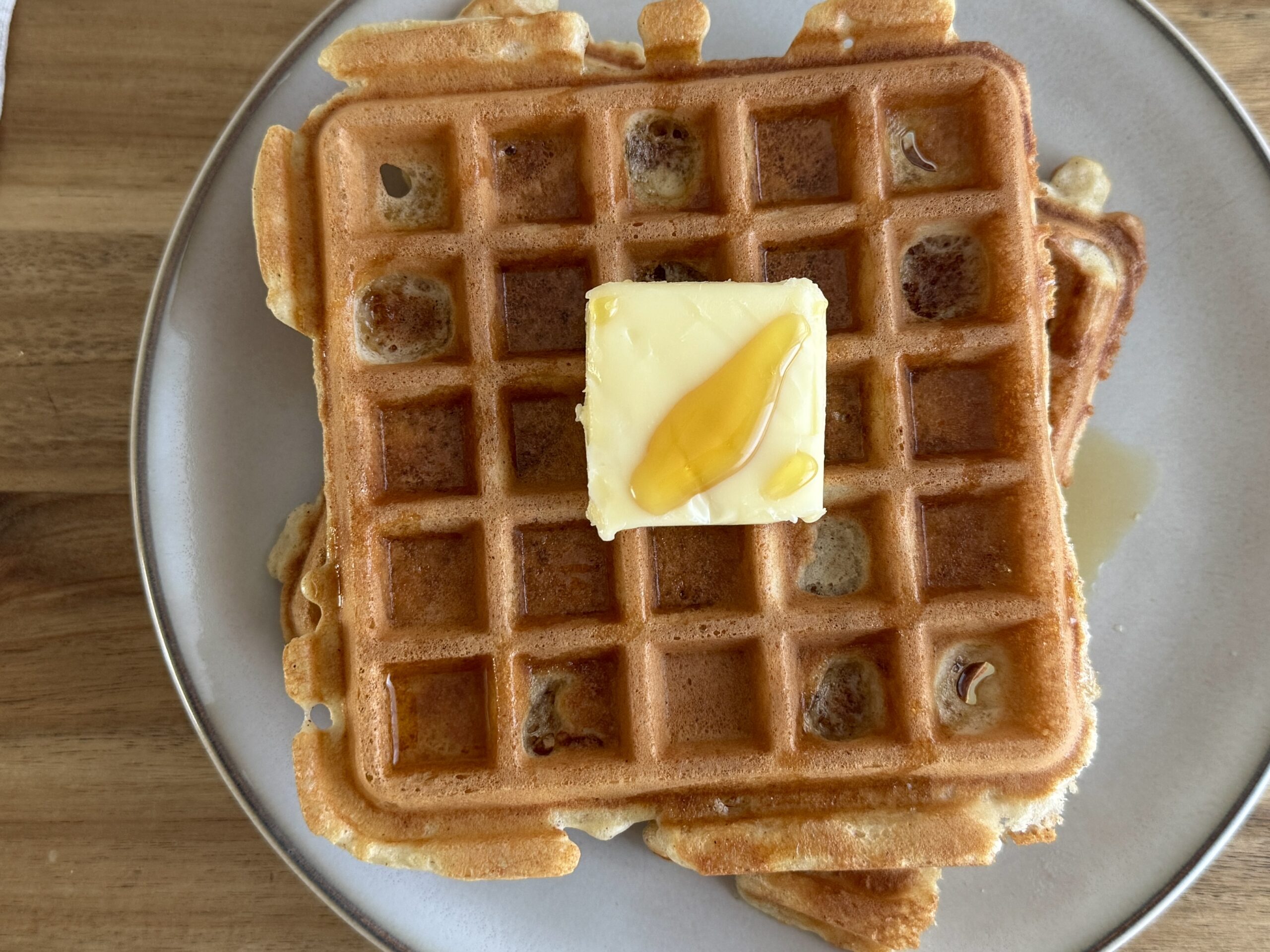 stacked sourdough discard waffles on a plate with a square of butter in the middle with maple syrup