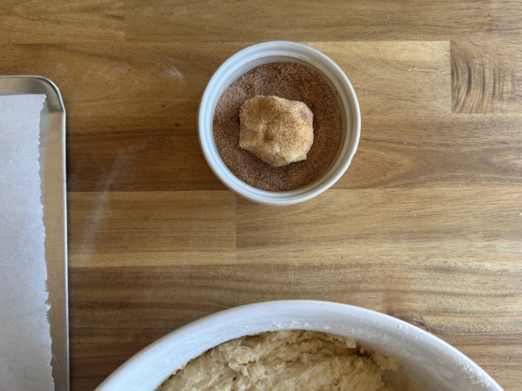 a white bowl of cinnamon and sugar with a ball of dough in it, getting coated before baking
