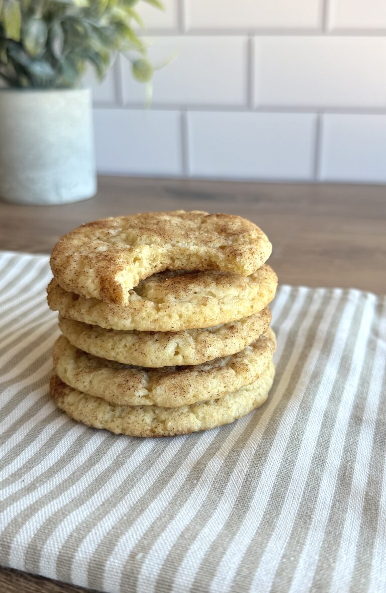 a stack of snickerdoodle cookies on a cloth on a wooden table. The top cookie has a bite out of it to show texture