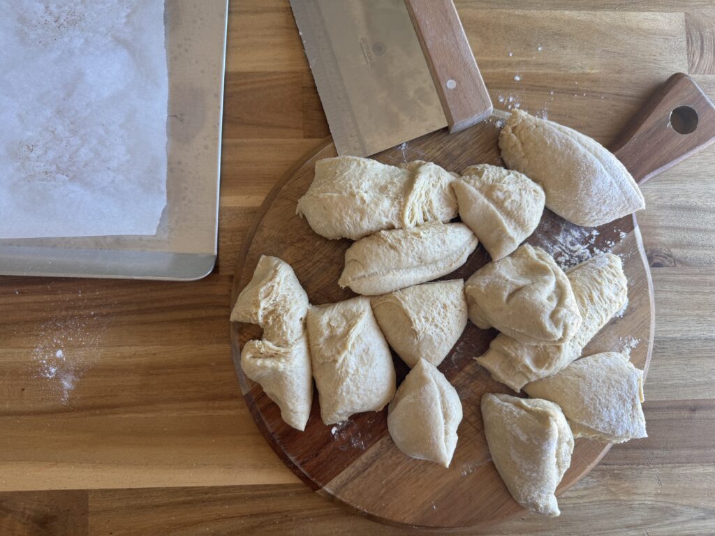 burger bun dough divided into 12 pieces on a wooden cutting board, ready to shape