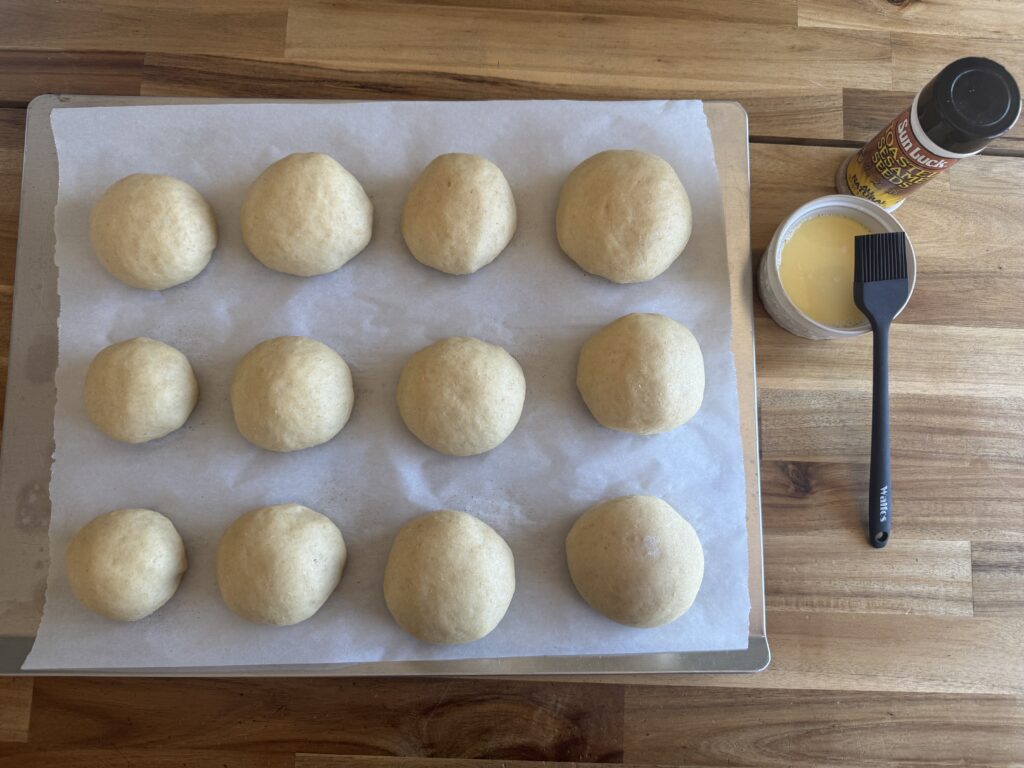 burger bun dough after second rise on a baking sheet with parchment paper lining it