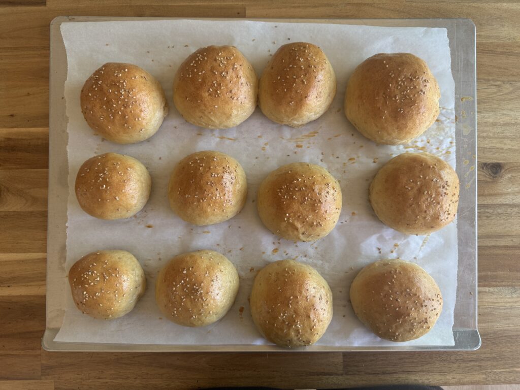 burger buns on a baking sheet lined with parchment paper, right out of the oven