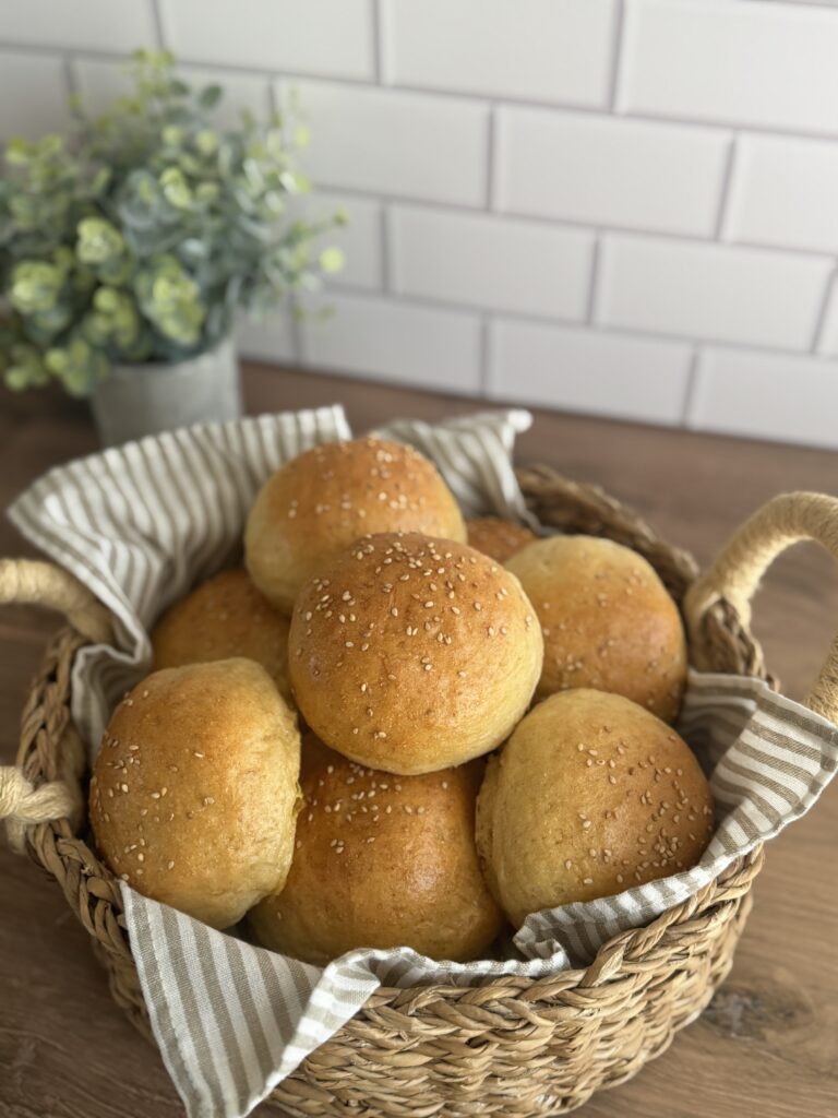 a bread basket full of sourdough discard buns, lined with a linen cloth on a wooden table with a white tile back splash