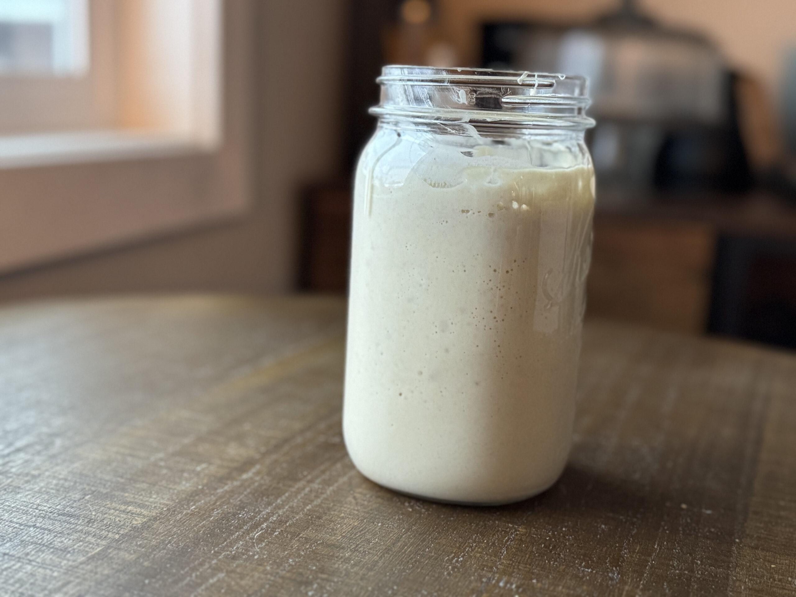 a jar of sourdough starter on a wooden table in a kitchen