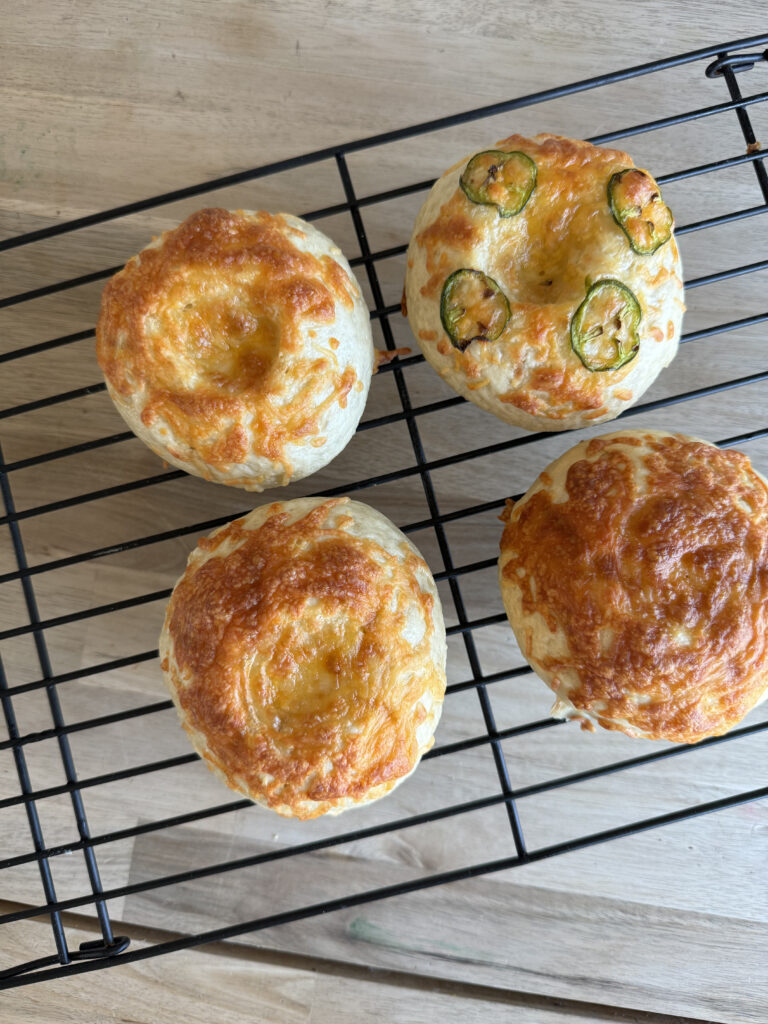 a drying rack of four bagels with cheddar and jalapeño on them.