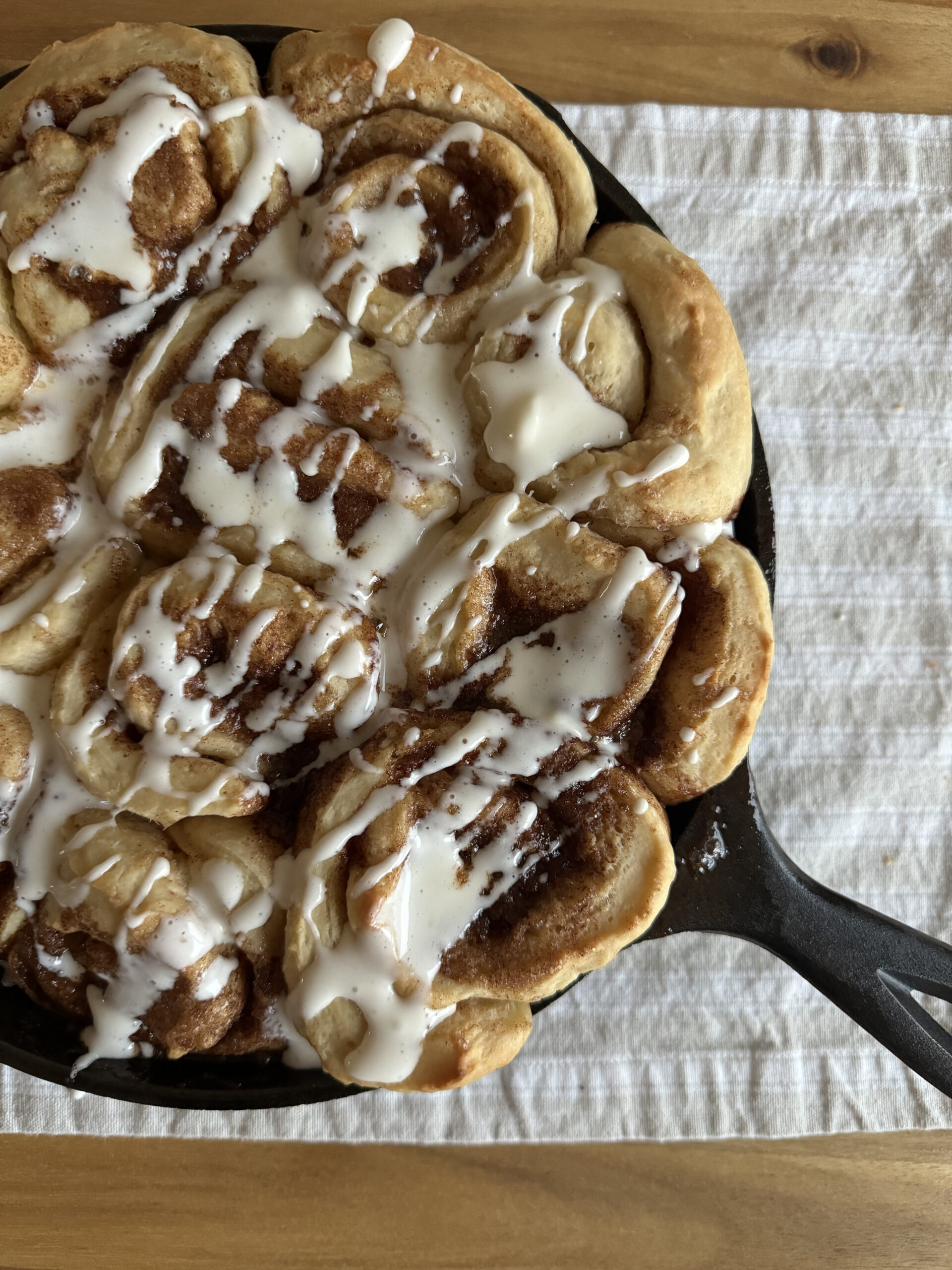 a cast iron pan of cinnamon rolls drizzled with frosting on a wooden table with a farmhouse table runner