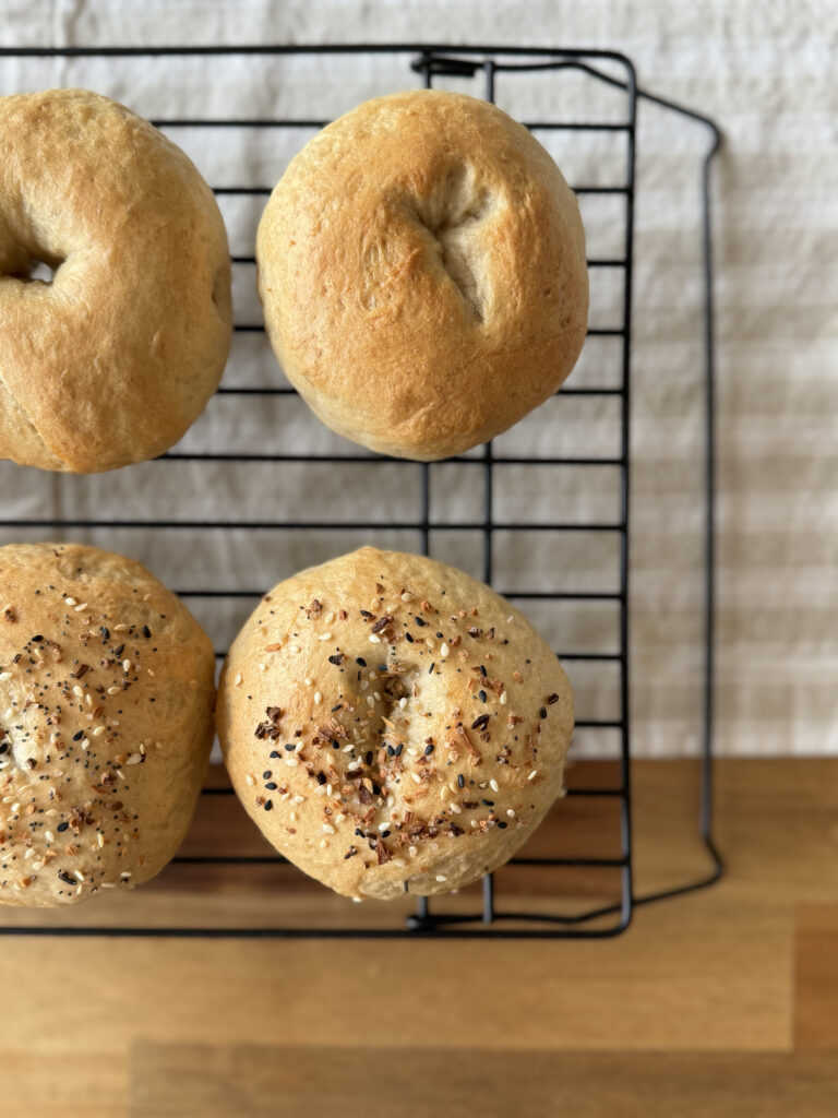 fresh out of the oven sourdough bagels on a cooling rack on a wooden table with a striped tan runner underneath