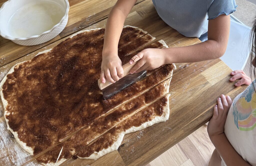 a girl cutting cinnamon roll strips on the table before rolling them up.