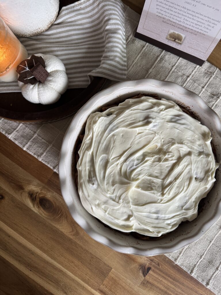 a ceramic white dish of cinnamon rolls smothered in cream cheese frosting, on a table decorated for fall