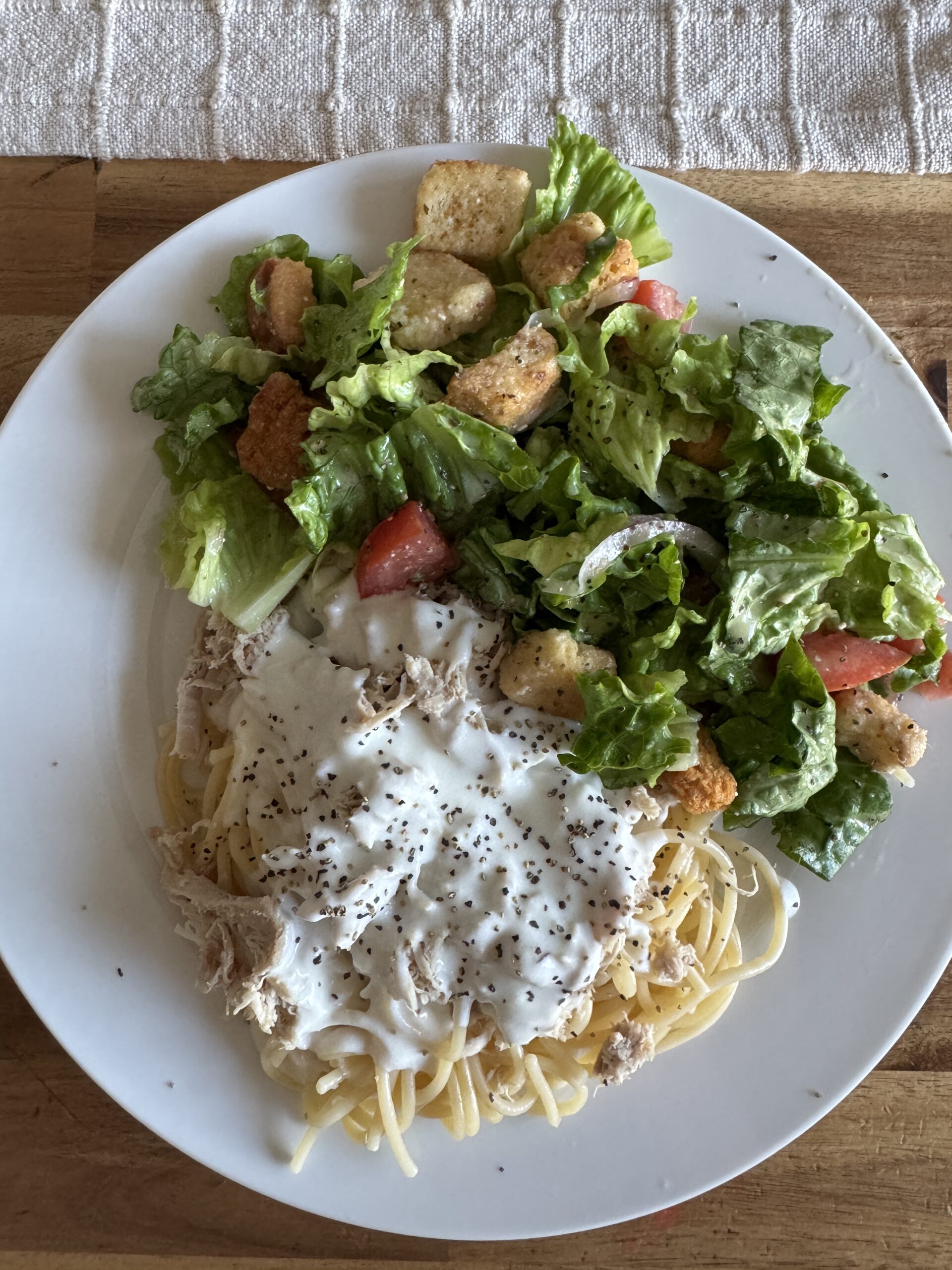 a plate of Alfredo sauce on noodles with a side of salad