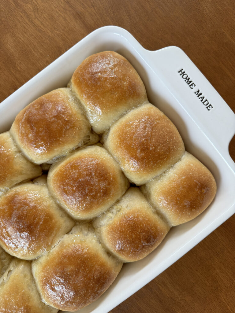 a white baking dish of homemade dinner rolls on a wooden table. Golden, buttered tops
